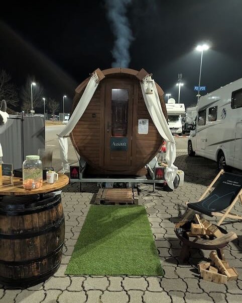 Mobile Fasssauna von Spalivo im abendlichen Event-Einsatz mit Liegestuhl und Holzfeuer
